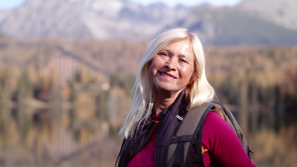 Active senior woman hiker standing outdoors in nature, looking at camera.