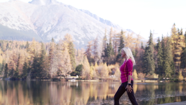 Active senior woman hiker standing outdoors by lake in nature, doing stretching.