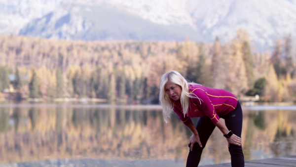 Active senior woman hiker standing outdoors by lake in nature, doing stretching. Slow motion.