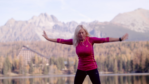 Active senior woman hiker standing outdoors by lake in nature, doing exercise. Slow motion.