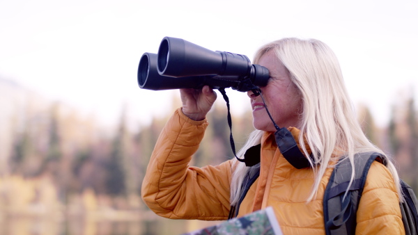 An active senior woman hiker with binoculars standing outdoors in nature. Slow motion.