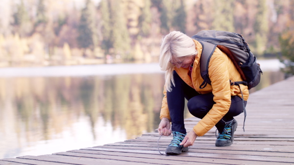 Happy senior woman hiker outdoors by lake in nature, tying shoelaces.