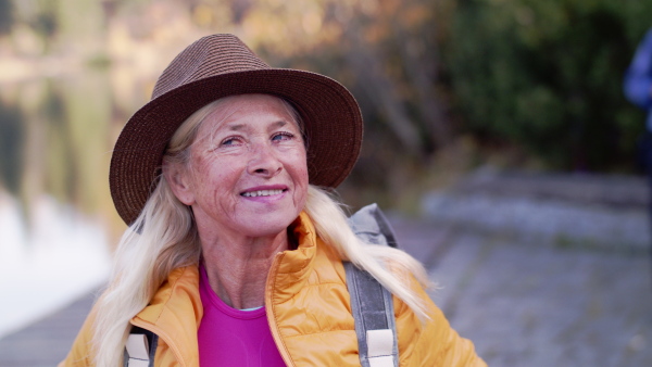 Front view portrait of active senior woman hiker standing outdoors in nature, looking around.