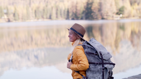 Side view of senior woman with backpack hiker standing outdoors by lake in nature.