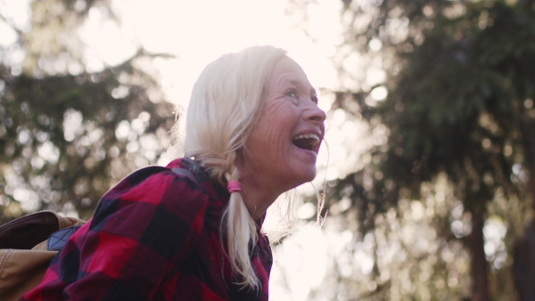 An active senior woman hiker standing outdoors in nature, laughing.