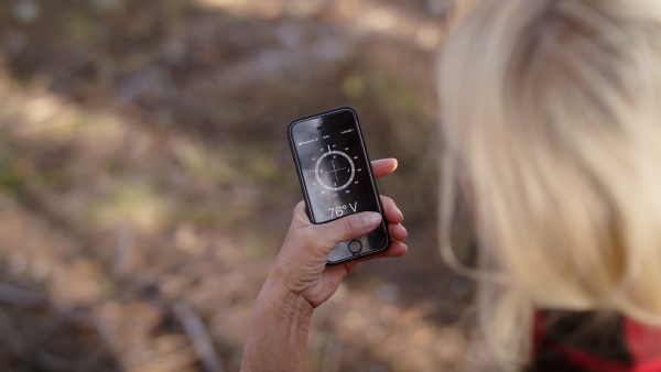 Senior woman hiker outdoors in nature, using compass on telephone. Slow motion.