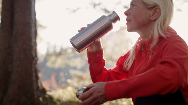 An active senior woman hiker outdoors in nature, drinking. Slow motion.