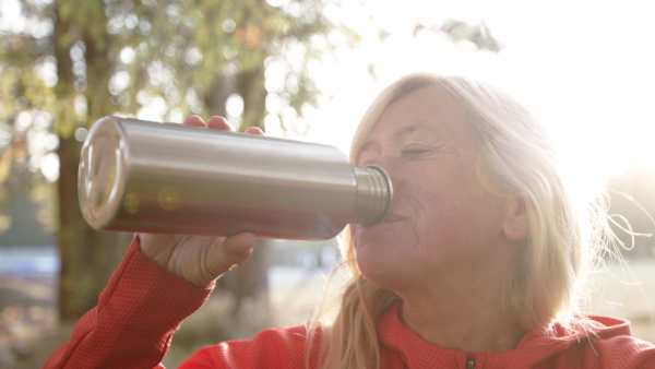 An active senior woman hiker outdoors in nature, drinking. Slow motion.