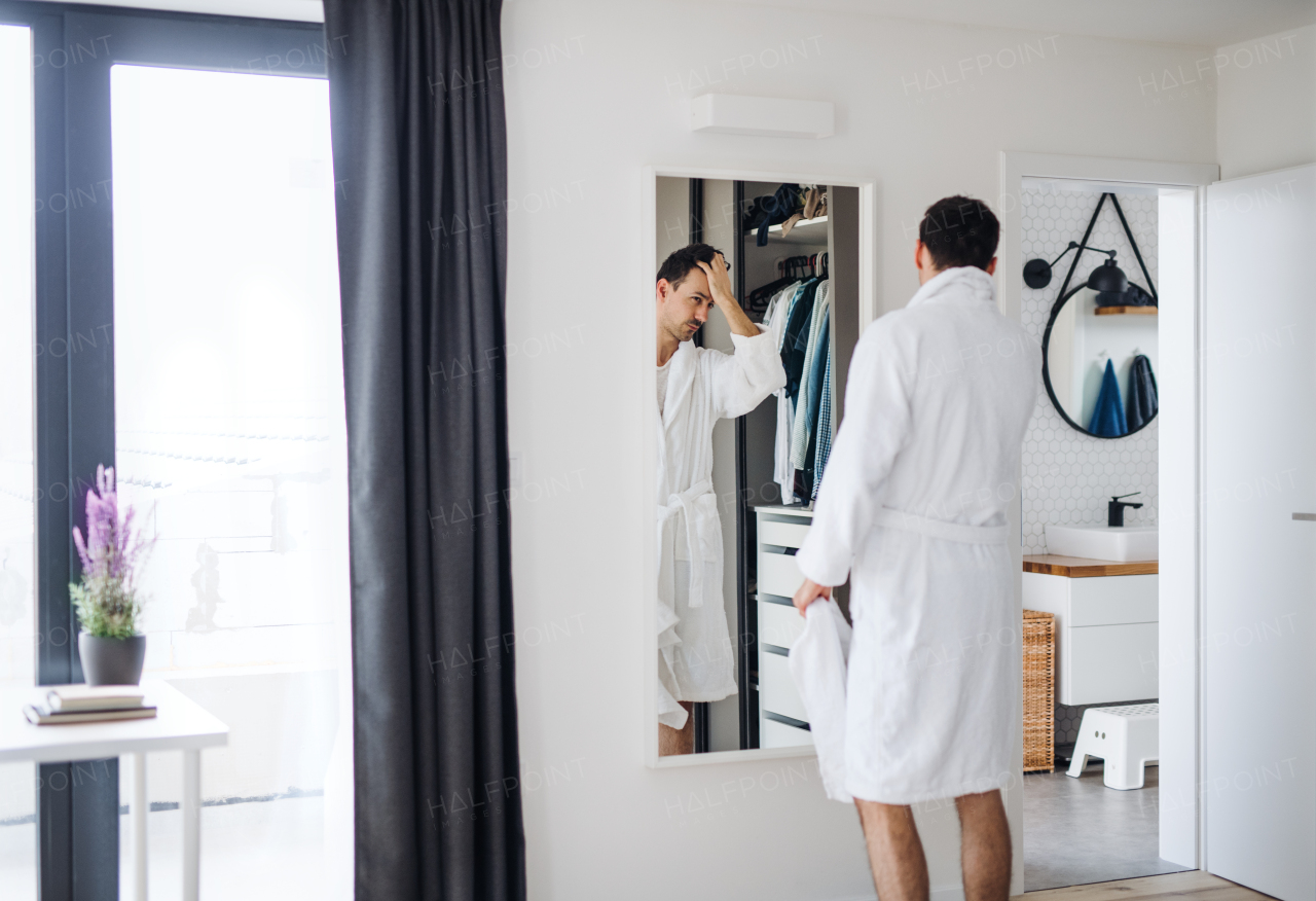 A young man looking in mirror in bedroom in the morning, daily routine.