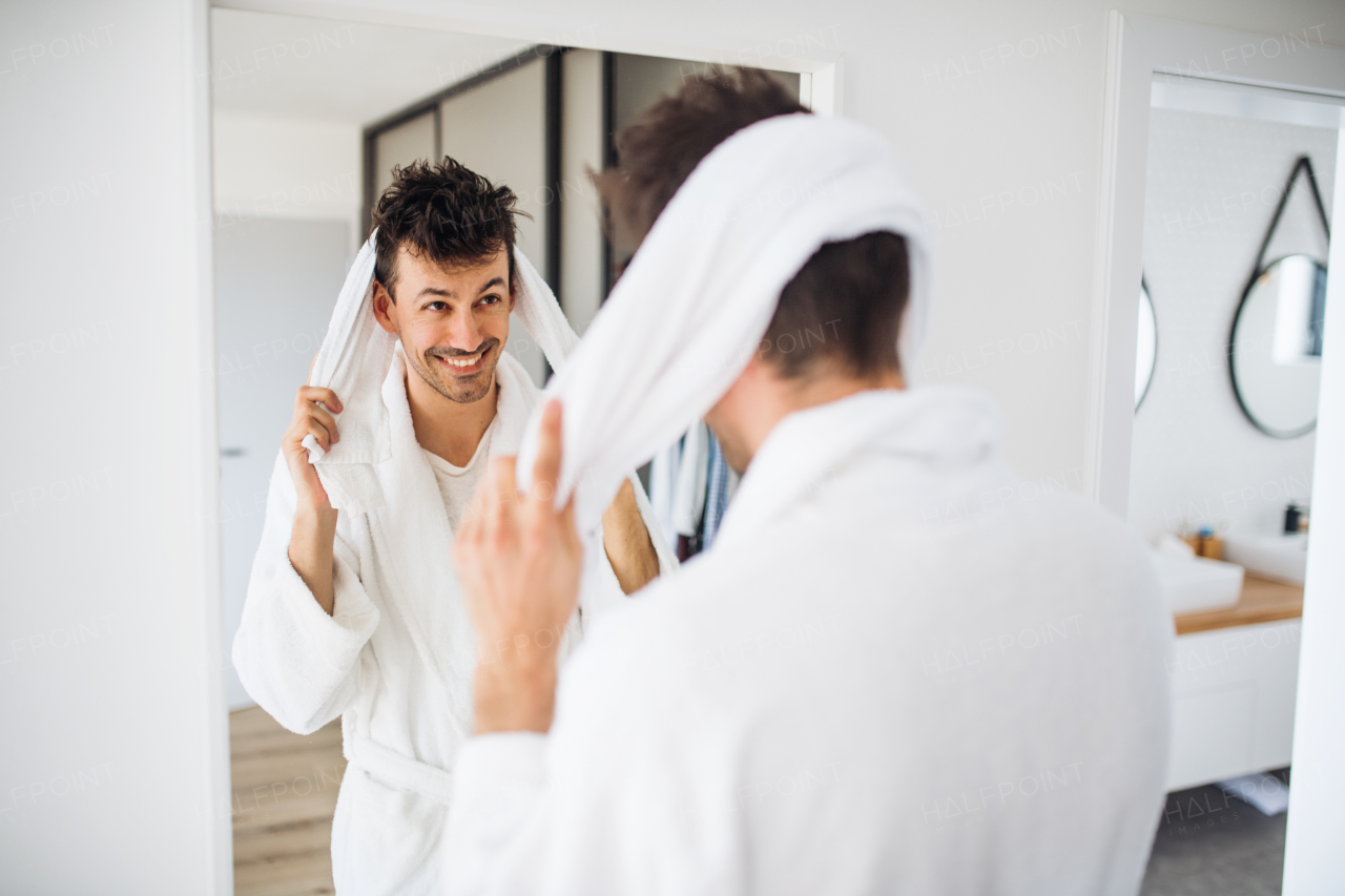 Young man with bathrobe drying hair in the bedroom, a morning routine.