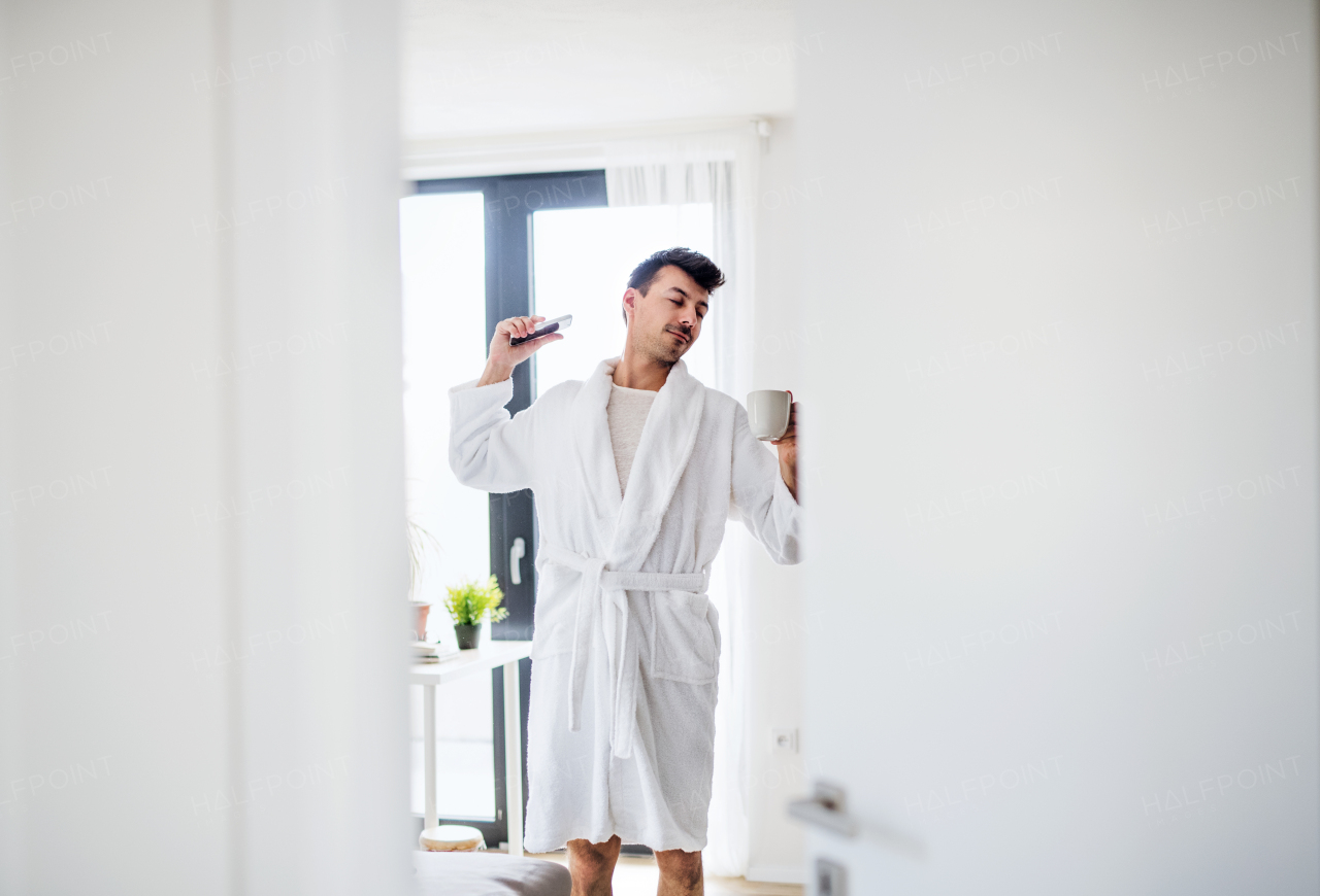 Young man with coffee and smartphone in the bedroom in the morning, stretching.