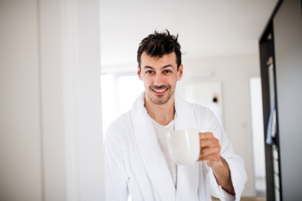 Front view of young man with coffee in the bedroom in the morning.