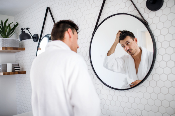 A young man looking in mirror in the bathroom in the morning, daily routine.