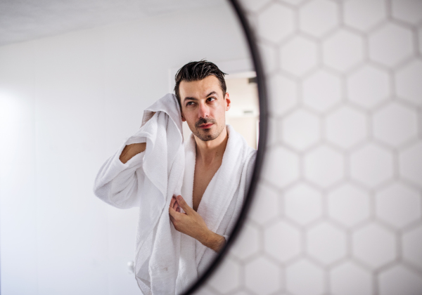 Young man in the bathroom in the morning routine, reflection in mirror. Copy space.