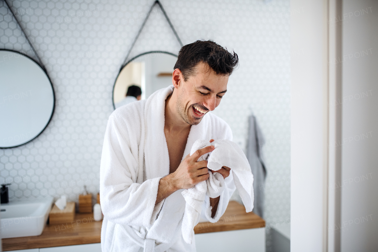 A young man with bathrobe laughing in the bedroom, a morning routine.