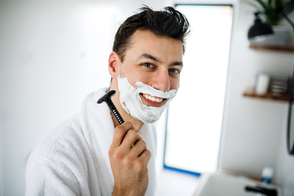 Young man with shaving foam on face in the bathroom in the morning, a daily routine.