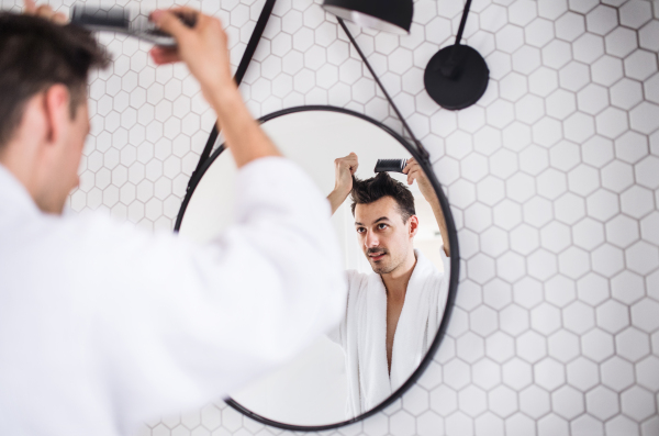 A young man looking in mirror in the bathroom in the morning, combing hair. A daily routine.