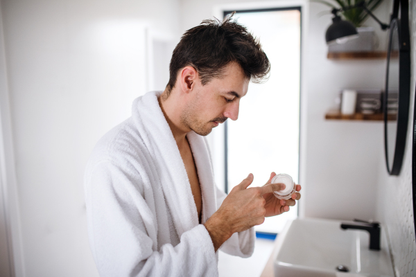 Young man putting cream on face in the bathroom in the morning, a daily routine.