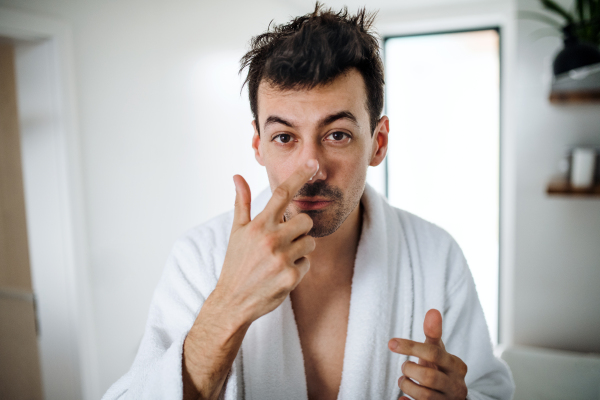 Young man putting cream on face in the bathroom in the morning, a daily routine.