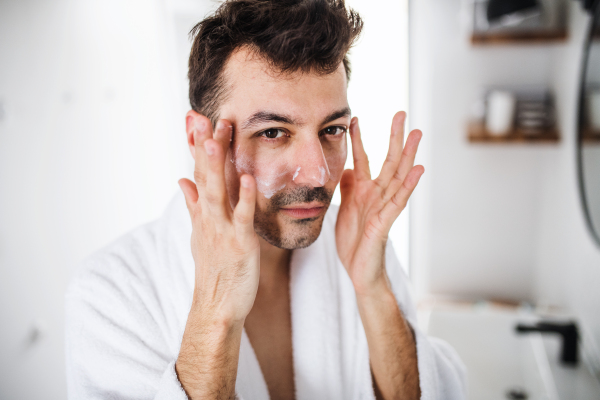 Young man putting cream on face in the bathroom in the morning, a daily routine.