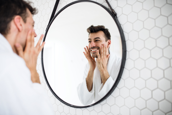 A young man looking in mirror in the bathroom in the morning, daily routine.