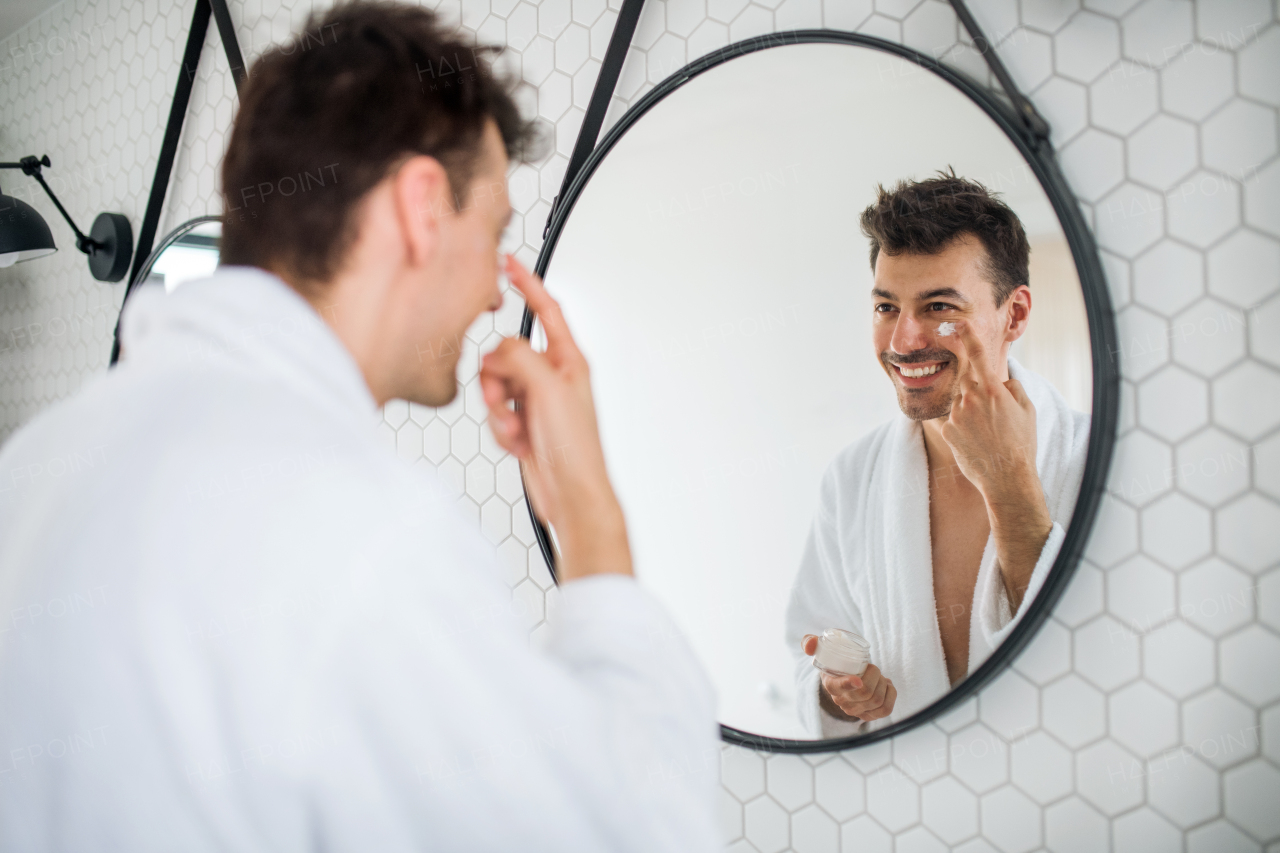 Young man putting cream on face in the bathroom in the morning, a daily routine.