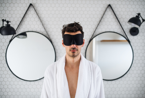 Young man with eye mask in the bathroom in the morning, standing.