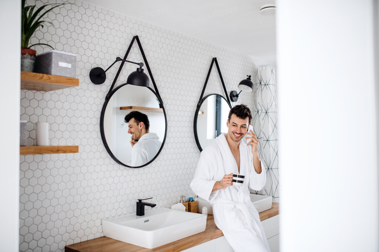 A young man with coffee and smartphone in the bedroom, a morning routine.