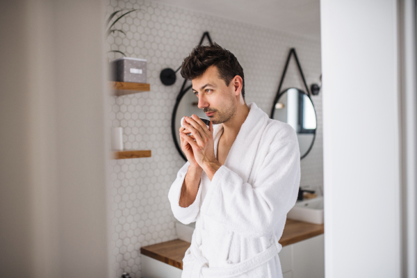 Young man standing in the bathroom in the morning, drinking coffee.