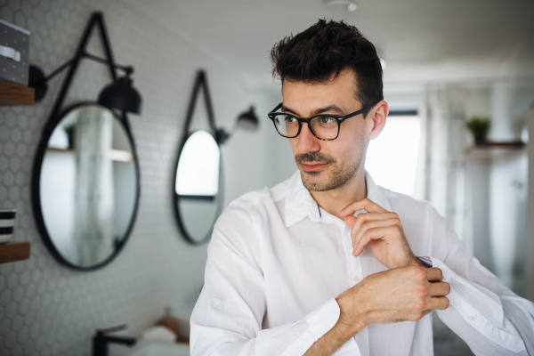 A young man putting on shirt in the bathroom in the morning.