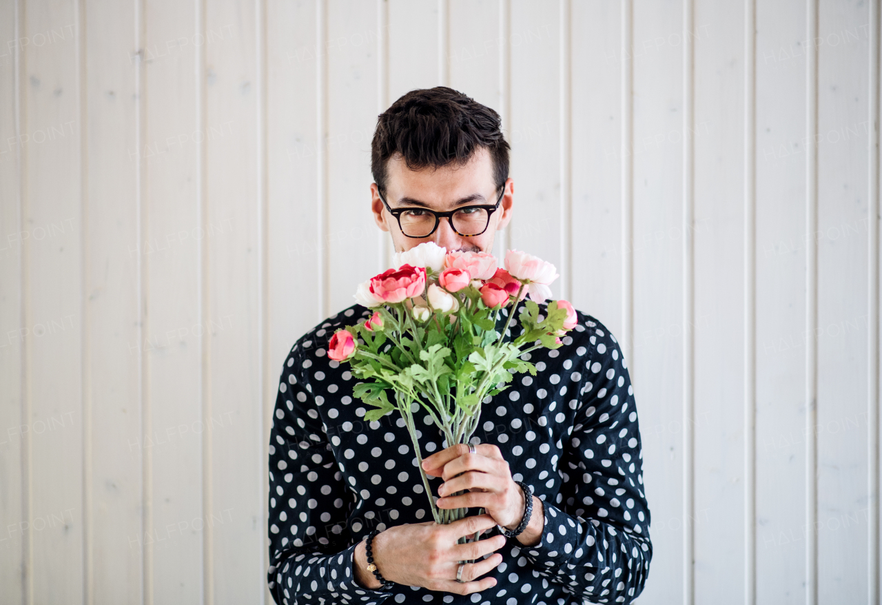 Handsome young man with flowers standing against white wooden background wall.