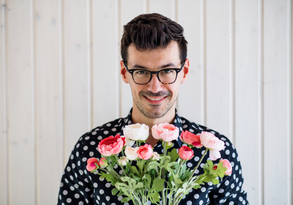 Handsome young man with flowers standing against white wooden background wall.