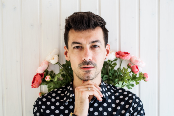 Handsome young man with flowers standing against white wooden background wall.