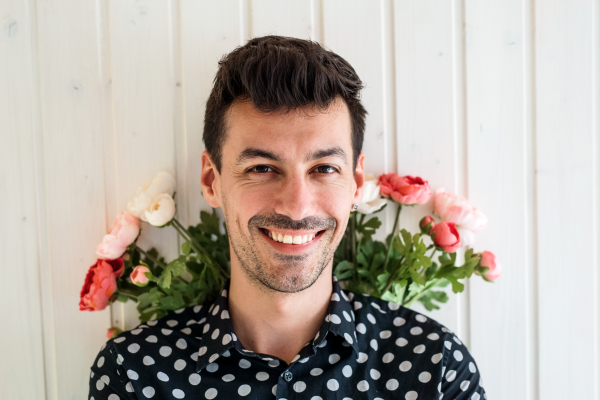 Handsome young man with flowers standing against white wooden background wall.