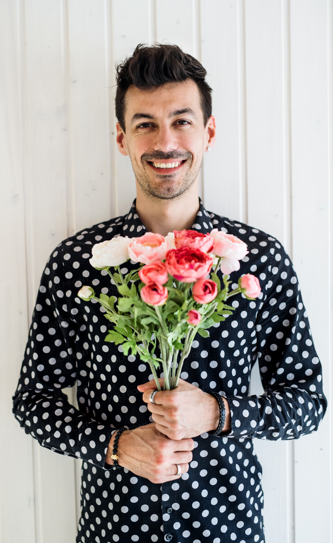 Handsome young man with flowers standing against white wooden background wall.