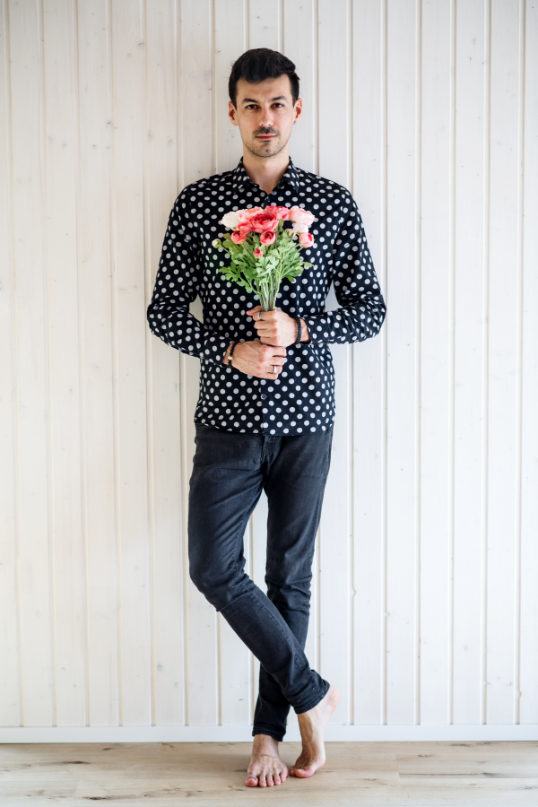 Handsome young man with flowers standing against white wooden background wall.