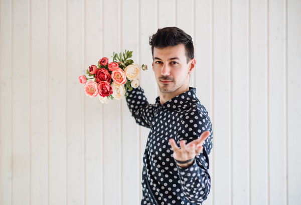 Handsome young man with flowers standing against white wooden background wall.