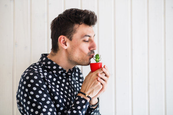 Young man standing against white wooden background wall, holding a small plant. Copy space.