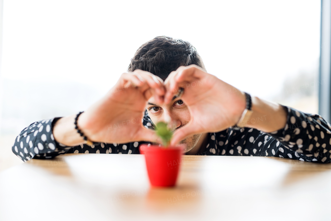 A young man in love small plant on table indoors at home.