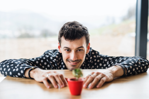 A young man looking at small plant on table indoors at home.