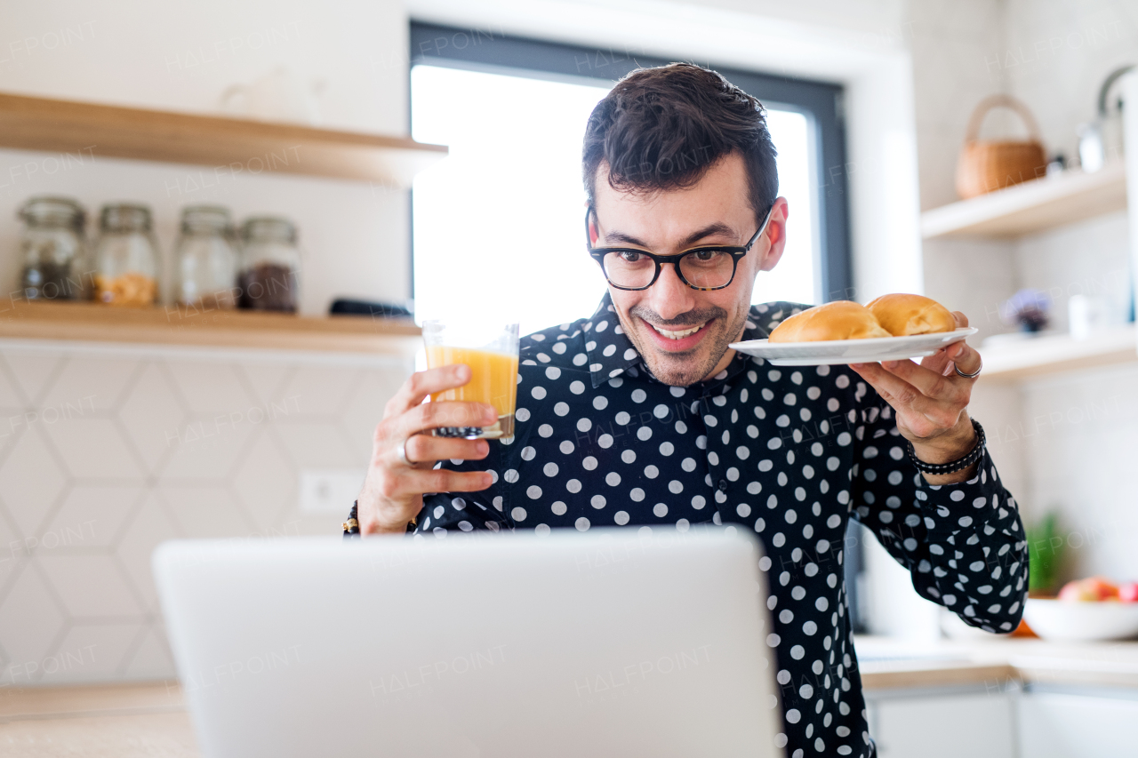 Young man with breakfast and laptop, working in a home office concept.