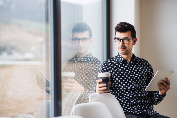 A young man with coffee and tablet sitting by the window. Copy space.