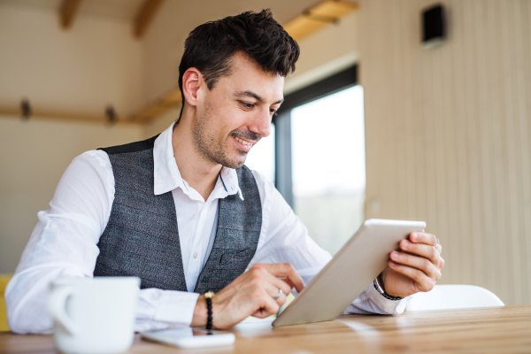 Young handsome man with coffee sitting at the table, using tablet.