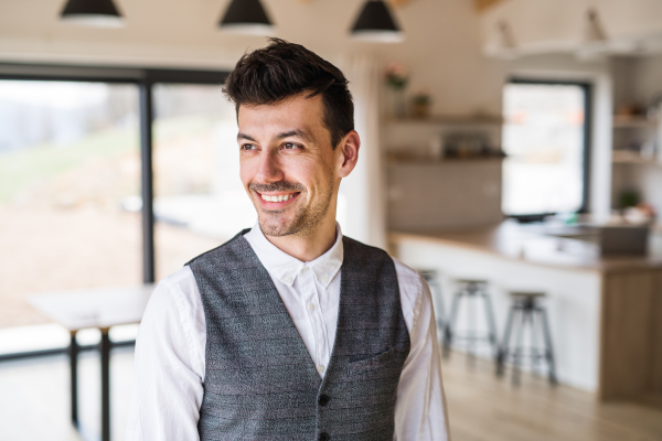 Front view portrait of young man standing indoors at home, laughing.