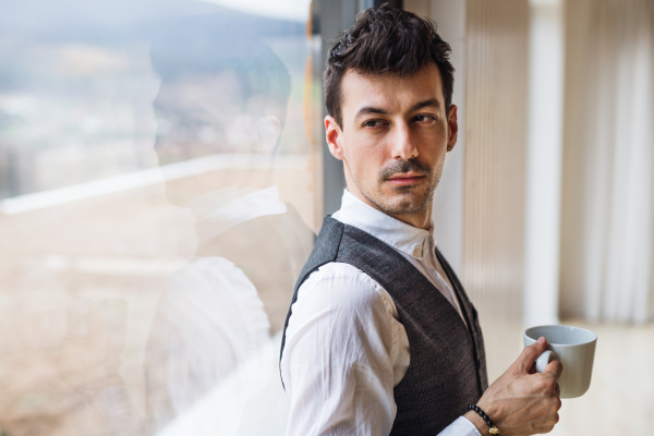 A young man with coffee standing by the window. Copy space.