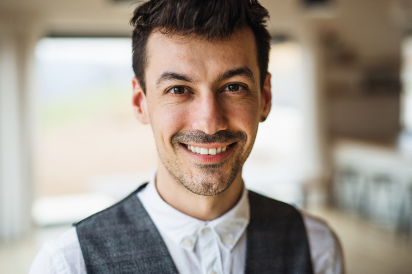 Front view portrait of young man standing indoors at home, looking at camera.