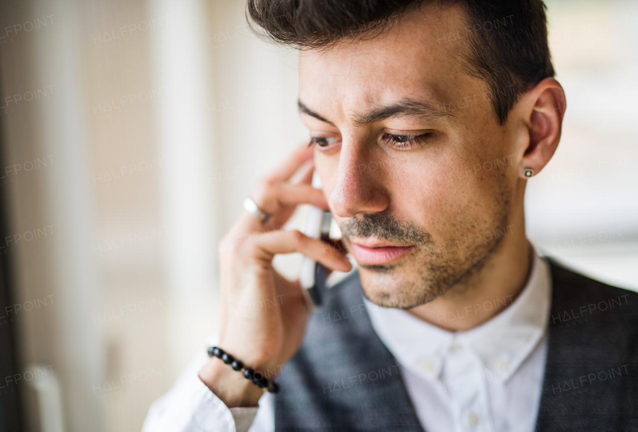 A young man with smartphone standing indoors at home, making a phone call.