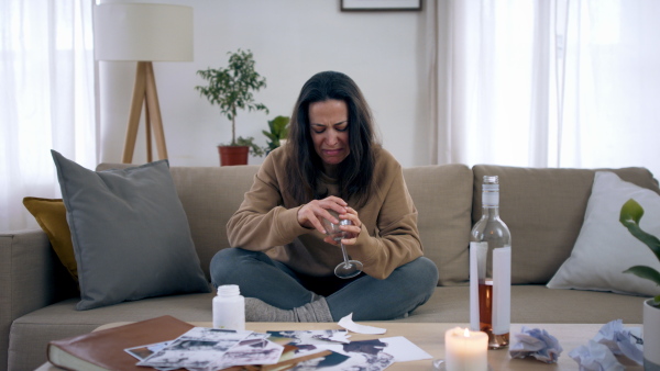 Front view of crying depressed woman drinking alcohol indoors, mental health concept.