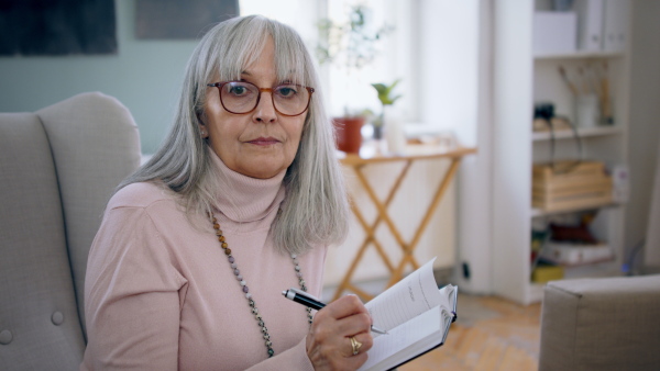 Senior therapist making notes and looking at camera indoors, mental health concept.