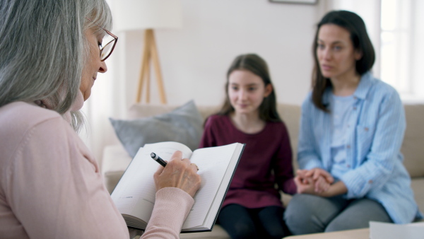 Sad and depressed small girl and mother talking to therapist indoors, mental health concept.